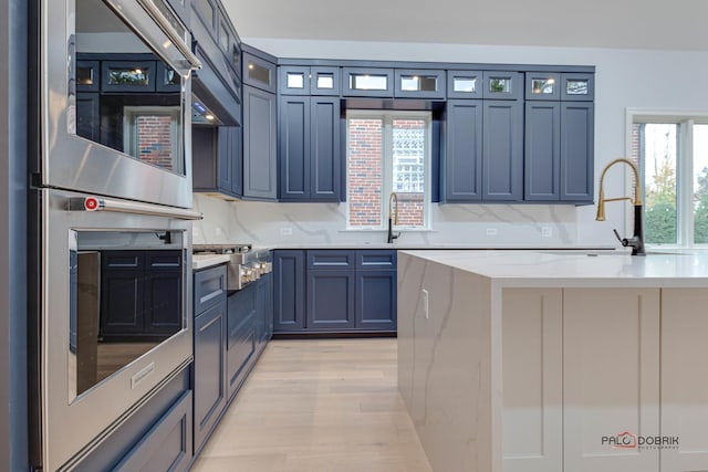 kitchen featuring glass insert cabinets, stainless steel gas cooktop, light wood-type flooring, decorative backsplash, and a sink