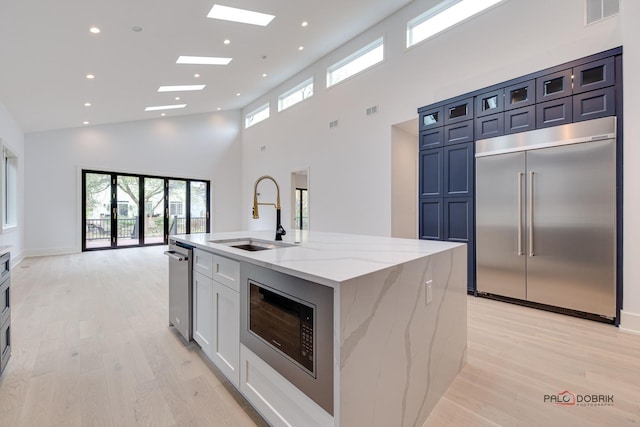 kitchen featuring visible vents, an island with sink, a sink, light wood-style floors, and built in appliances