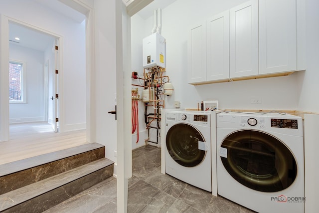 clothes washing area featuring baseboards, cabinet space, water heater, marble finish floor, and independent washer and dryer