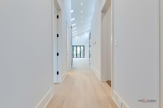 hall with a high ceiling, recessed lighting, light wood-style floors, and baseboards