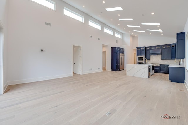 living room with visible vents, baseboards, a high ceiling, recessed lighting, and light wood-style floors