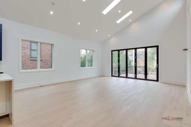 unfurnished living room with light wood-type flooring, baseboards, high vaulted ceiling, and a skylight