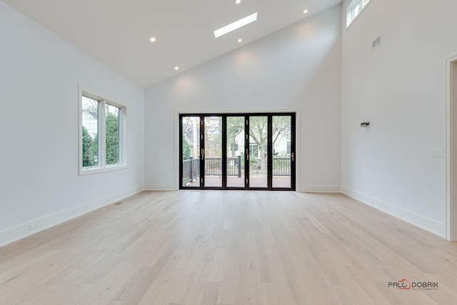 unfurnished room with a wealth of natural light, visible vents, a skylight, and light wood-style floors