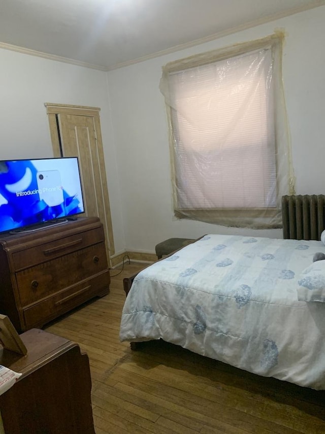 bedroom with radiator heating unit, wood finished floors, and crown molding