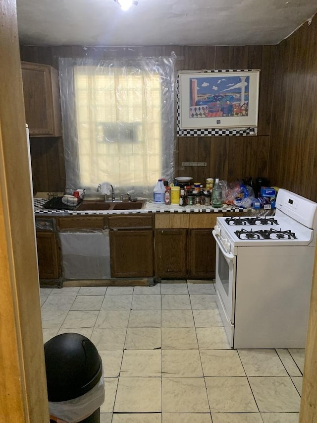 kitchen with wood walls, white gas range, a sink, and light tile patterned flooring