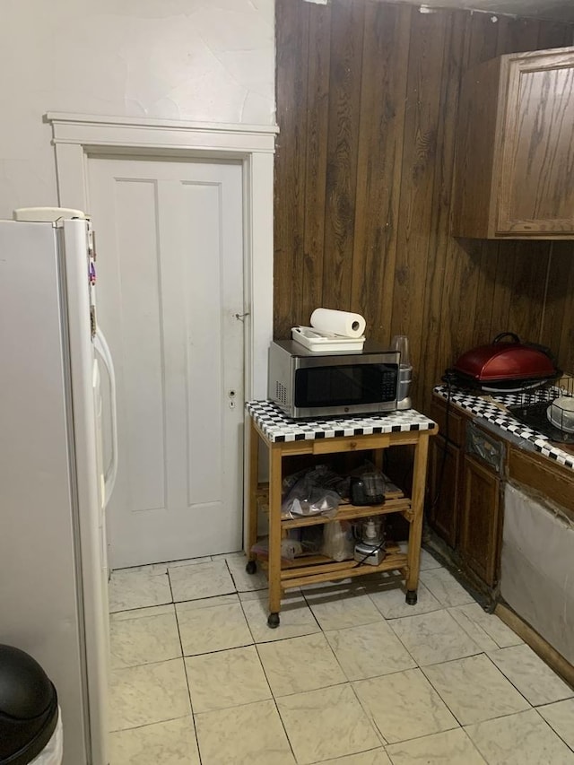 kitchen with light tile patterned floors, stainless steel microwave, and freestanding refrigerator