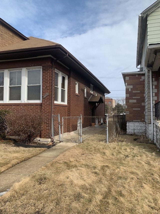 view of side of property featuring a yard, brick siding, fence, and a gate