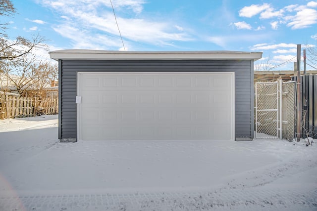 snow covered garage with a detached garage and fence