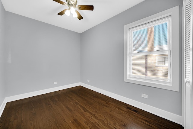 spare room with dark wood-style floors, a ceiling fan, visible vents, and baseboards