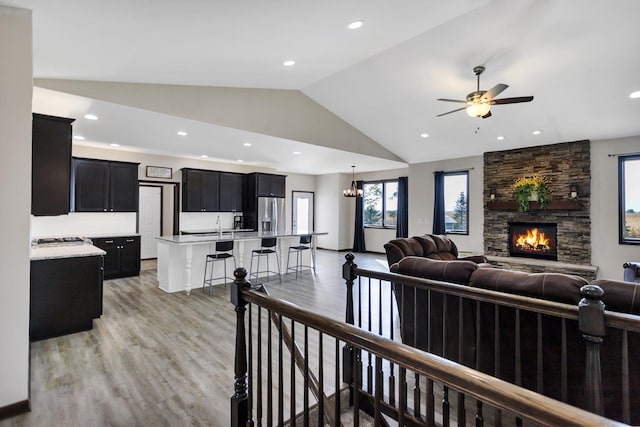 living room featuring high vaulted ceiling, a stone fireplace, recessed lighting, a ceiling fan, and light wood-style floors