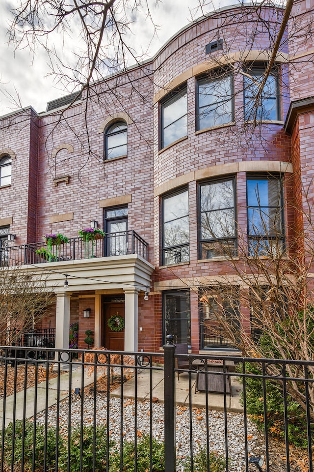 view of front facade with brick siding, a fenced front yard, and a balcony