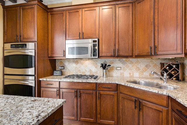 kitchen featuring light stone counters, brown cabinets, backsplash, appliances with stainless steel finishes, and a sink