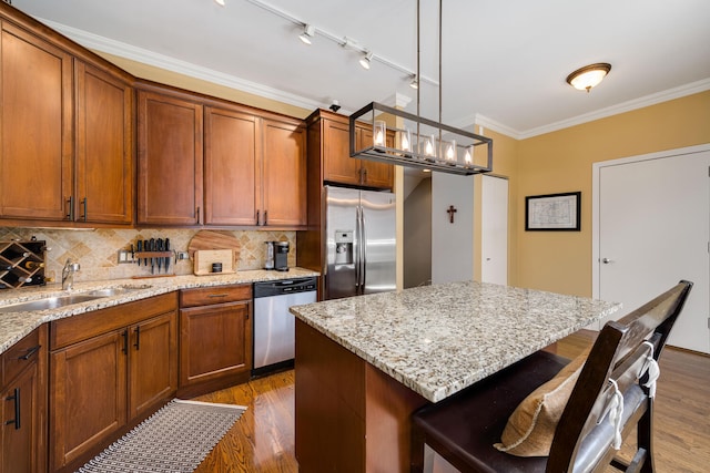 kitchen featuring stainless steel appliances, ornamental molding, a sink, wood finished floors, and a kitchen bar