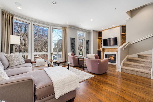 living room with recessed lighting, ornamental molding, a glass covered fireplace, wood finished floors, and stairs