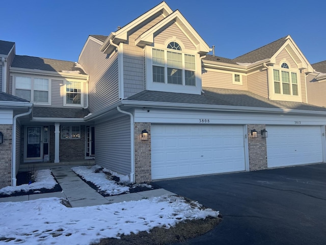 view of front of home featuring an attached garage, driveway, roof with shingles, and brick siding