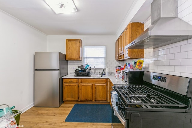 kitchen with wall chimney exhaust hood, brown cabinets, stainless steel appliances, light countertops, and a sink