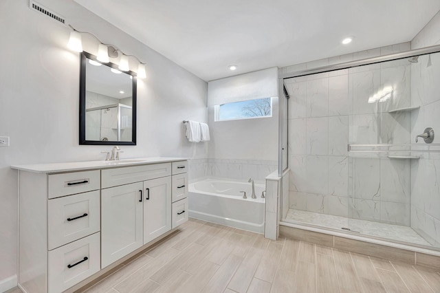 full bath with wood finish floors, a garden tub, visible vents, a stall shower, and vanity