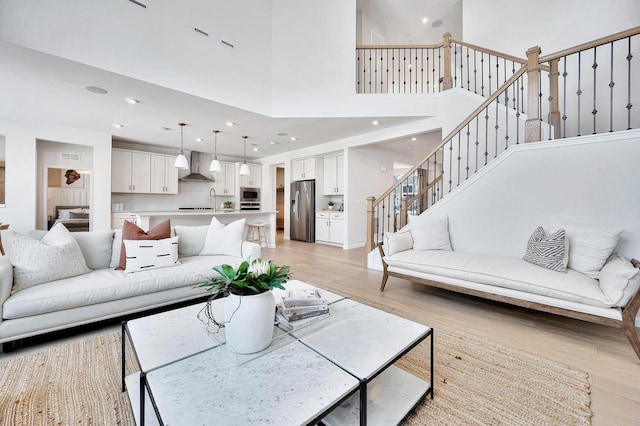 living area featuring light wood finished floors, visible vents, stairway, a high ceiling, and recessed lighting