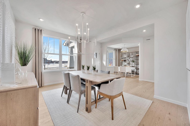 dining area featuring light wood finished floors, plenty of natural light, a chandelier, and baseboards