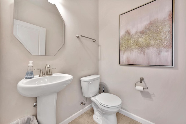 half bath with toilet, a sink, baseboards, and wood finished floors