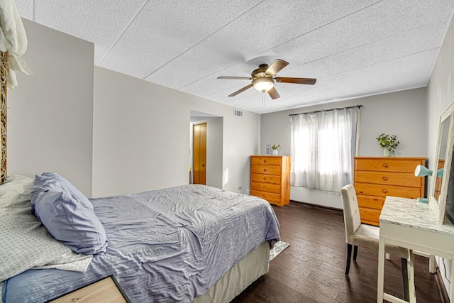 bedroom with ceiling fan, a textured ceiling, dark wood finished floors, and visible vents