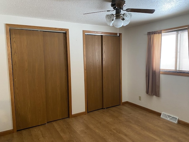 unfurnished bedroom featuring light wood finished floors, two closets, visible vents, a textured ceiling, and baseboards