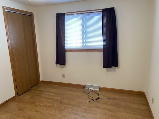 unfurnished bedroom featuring baseboards, a closet, visible vents, and light wood-style floors