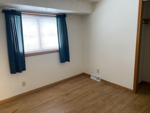 empty room with wood finished floors, visible vents, and baseboards