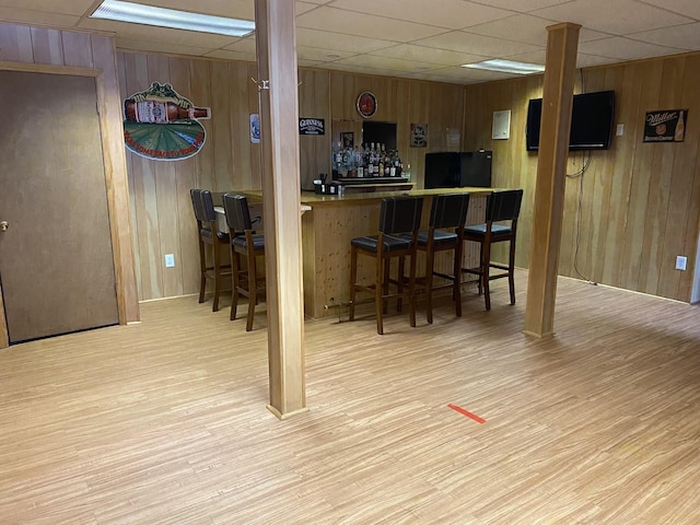 bar with a dry bar, wood walls, and light wood-style flooring