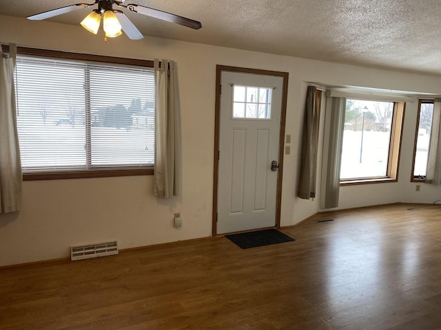 entrance foyer with a textured ceiling, plenty of natural light, wood finished floors, and visible vents