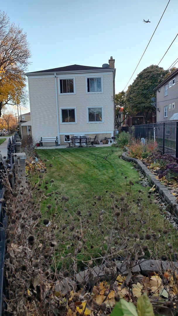 rear view of house with a chimney, fence, and a lawn