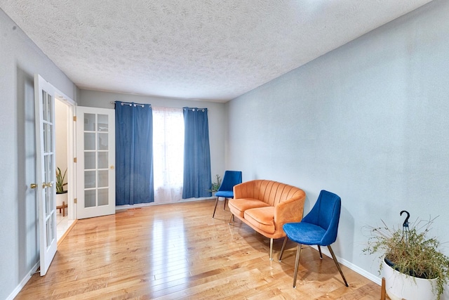 sitting room featuring a textured ceiling, french doors, light wood-type flooring, and baseboards