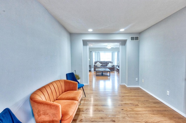 living area with light wood-style floors, visible vents, a textured ceiling, and baseboards