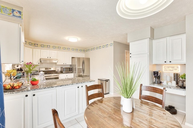 kitchen featuring appliances with stainless steel finishes, light stone counters, a peninsula, under cabinet range hood, and white cabinetry