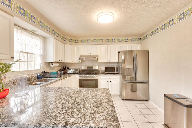 kitchen featuring under cabinet range hood, white cabinetry, appliances with stainless steel finishes, and a sink