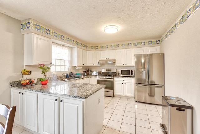 kitchen featuring a peninsula, under cabinet range hood, appliances with stainless steel finishes, and white cabinets