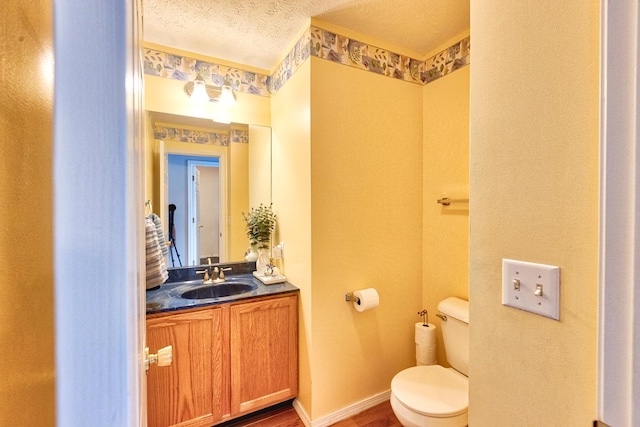 half bathroom with toilet, a textured ceiling, vanity, wood finished floors, and baseboards