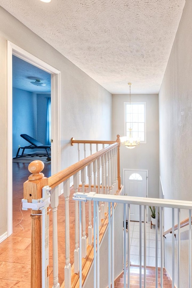 stairway with baseboards, a textured ceiling, an inviting chandelier, and wood finished floors