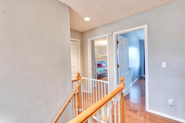 corridor featuring a textured ceiling, wood finished floors, an upstairs landing, and baseboards