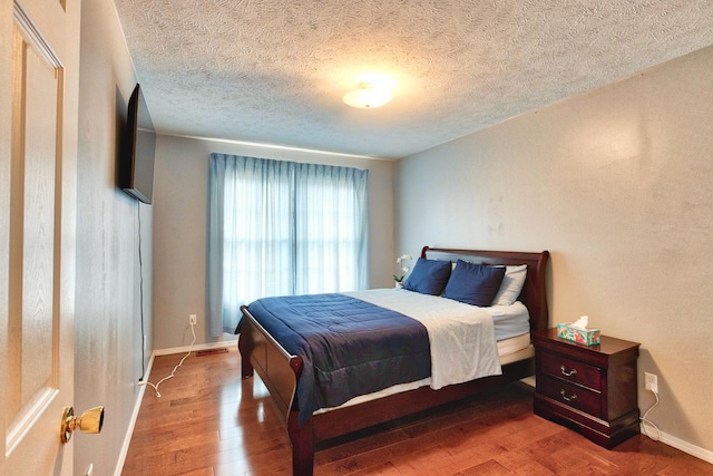 bedroom with a textured ceiling, wood finished floors, and baseboards