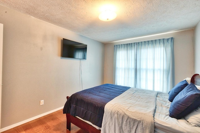 bedroom with a textured ceiling, wood finished floors, and baseboards