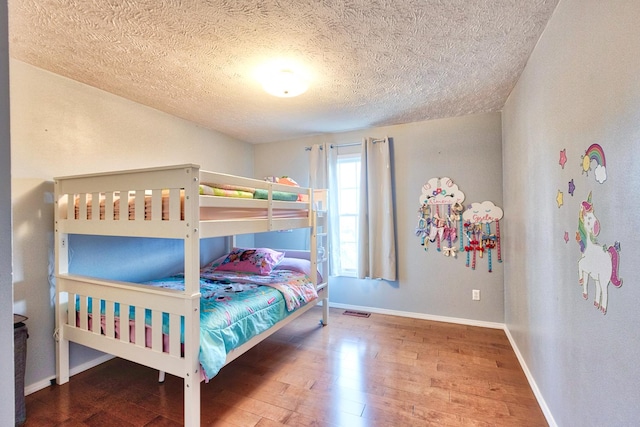 bedroom featuring a textured ceiling, wood finished floors, visible vents, and baseboards