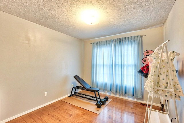 exercise area featuring a textured ceiling, wood finished floors, and baseboards