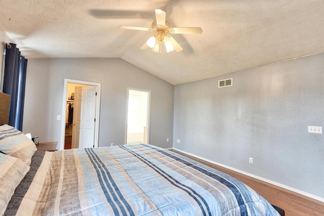 bedroom with baseboards, visible vents, wood finished floors, vaulted ceiling, and a textured ceiling