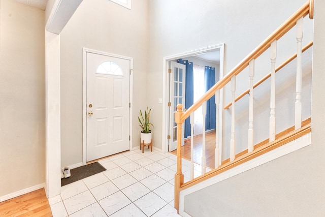 foyer entrance featuring a high ceiling, stairway, baseboards, and light tile patterned flooring