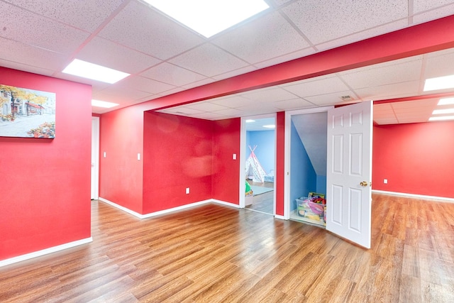 finished below grade area with a paneled ceiling, baseboards, and wood finished floors