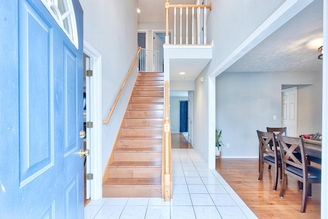 foyer with light wood-type flooring, stairs, baseboards, and a towering ceiling