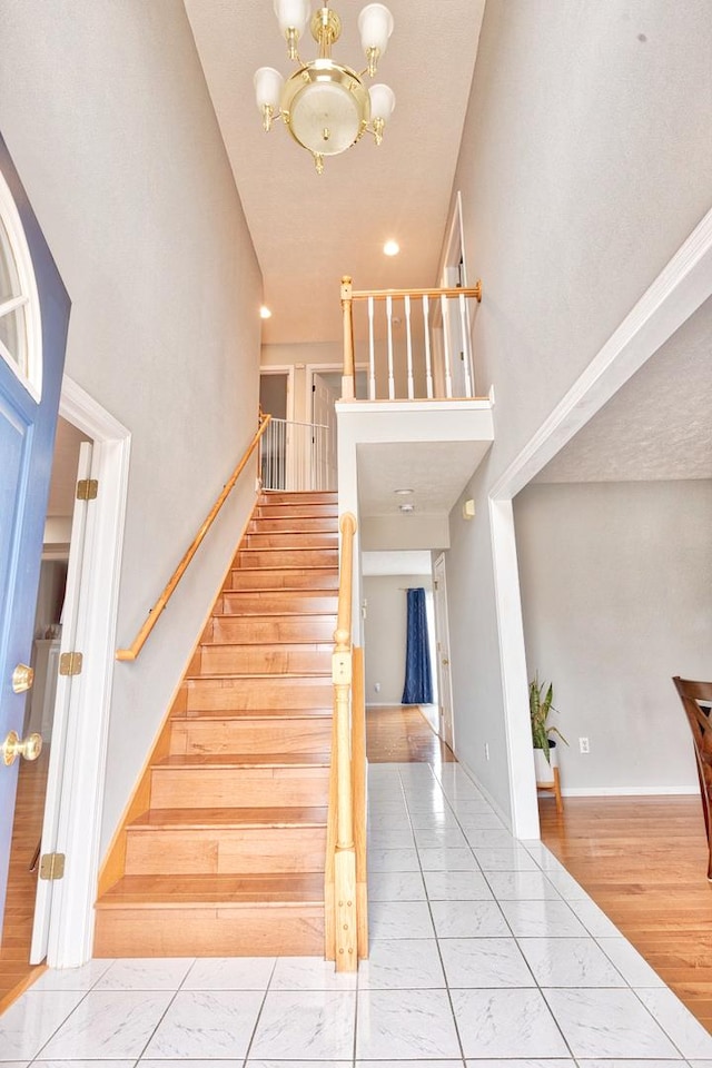 stairs with baseboards, wood finished floors, a towering ceiling, and an inviting chandelier