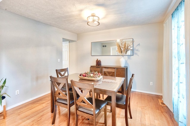 dining space featuring light wood-style flooring, visible vents, baseboards, and a textured ceiling