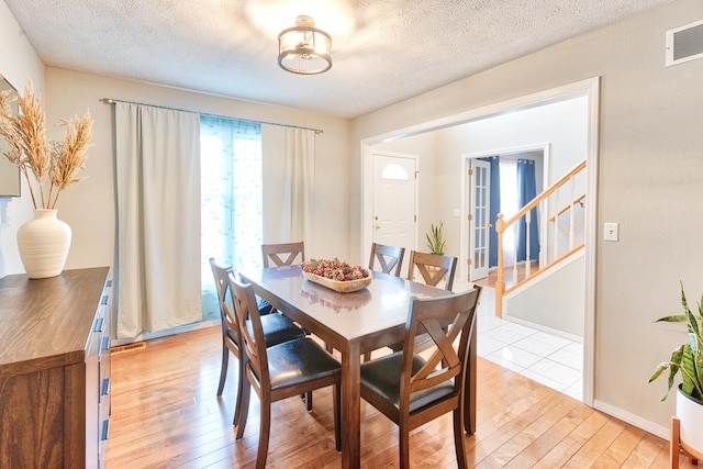 dining room with visible vents, baseboards, light wood-style flooring, stairway, and a textured ceiling